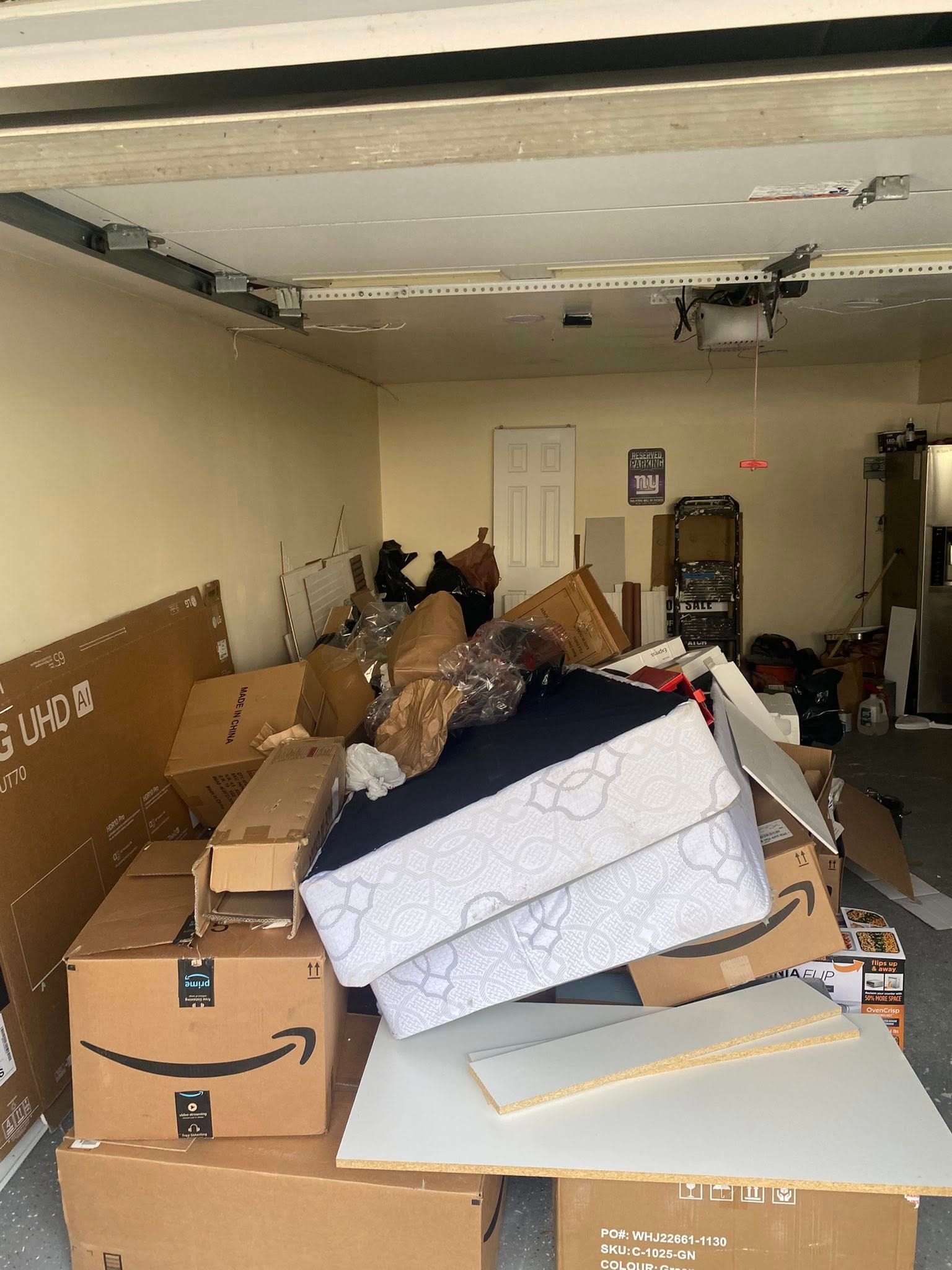 A messy garage filled with cardboard boxes, a mattress, and various household items piled in the center.