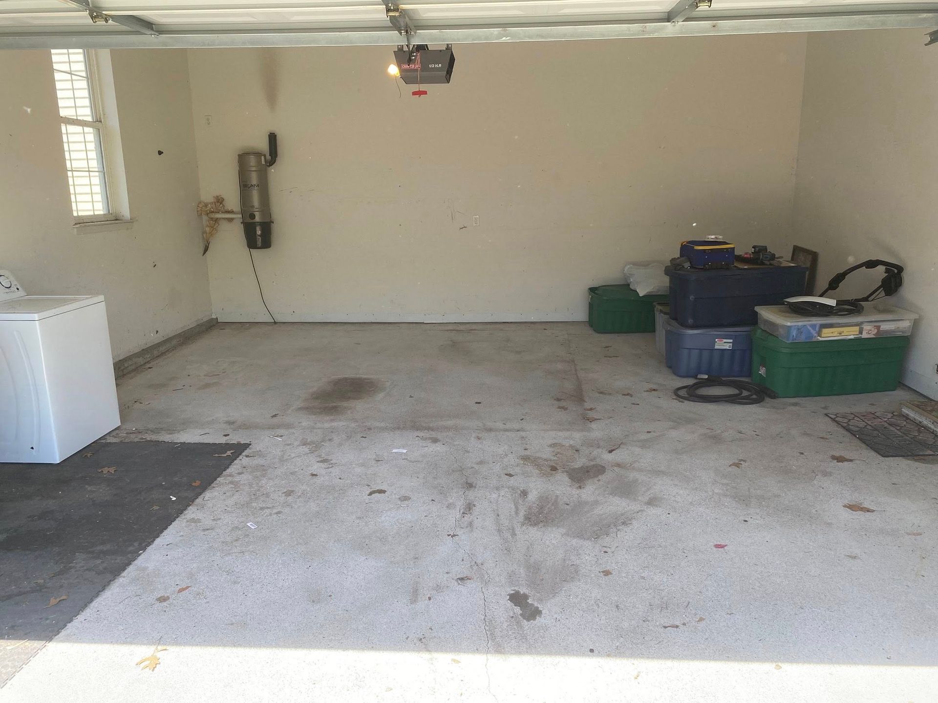 A garage interior with a concrete floor, a white appliance on the left, and storage bins piled against the right wall.