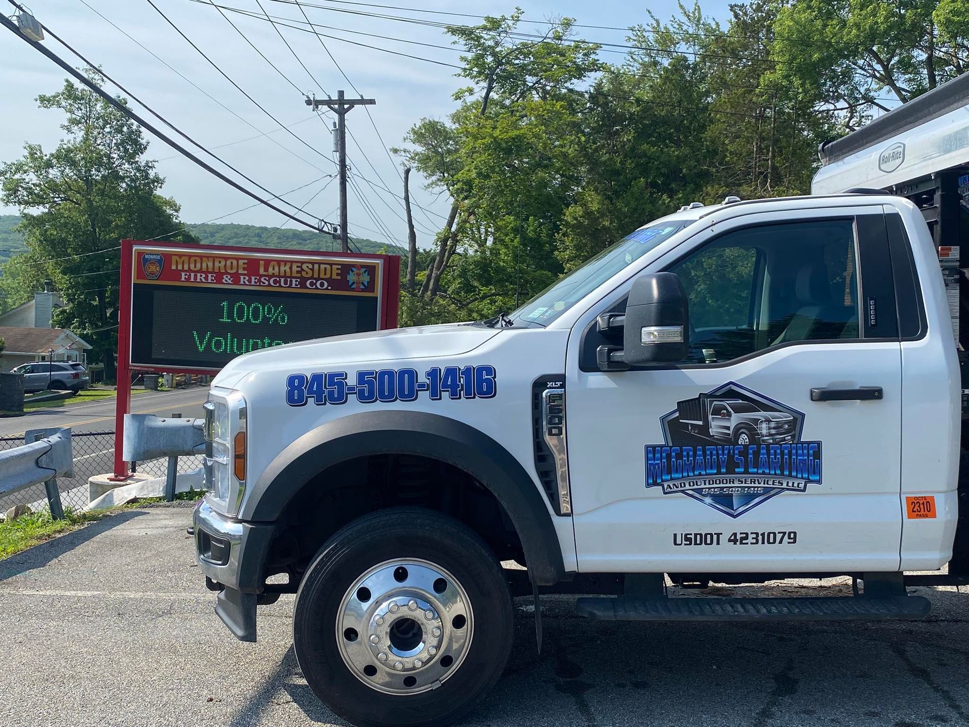 A white work truck parked in a lot next to a digital community sign under a clear blue sky.