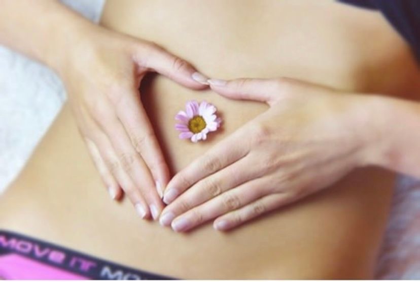 Hands framing a pink flower on a bare stomach, with a patterned waistband visible