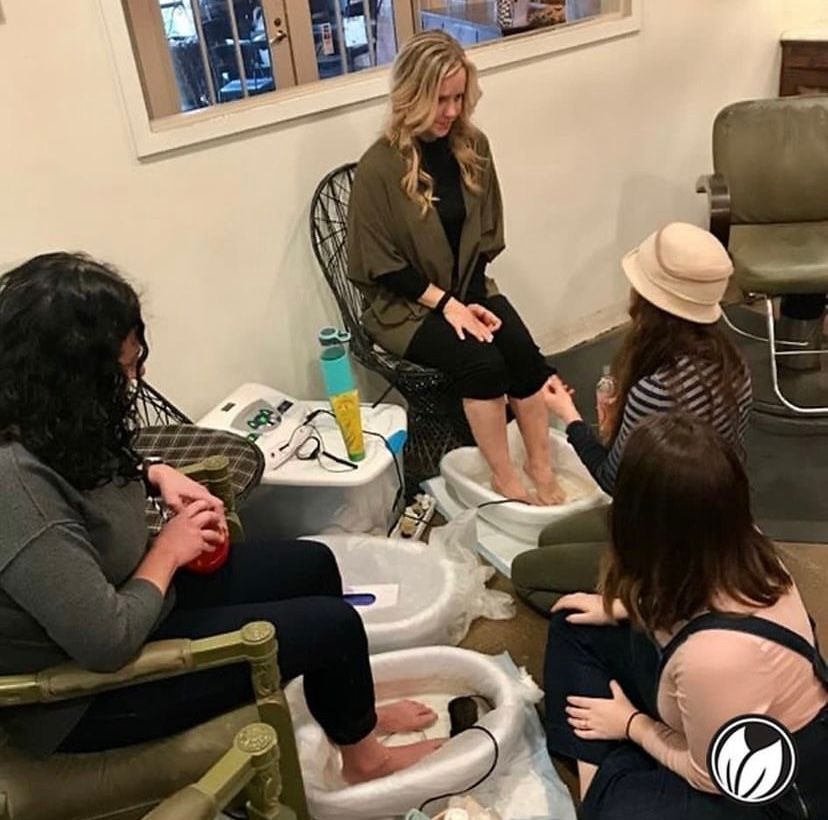 Pedicure spa with four people seated around foot baths, one woman getting a foot treatment in a salon room