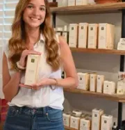 Smiling woman holding a boxed product in a shop with shelves of packaged items behind her