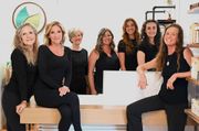 Group of six people seated and standing in a bright salon, smiling at the camera.