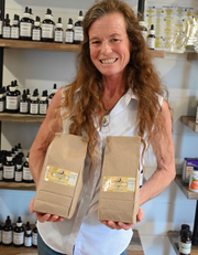 Woman smiling and holding two brown paper bags in a shop with shelves of bottles behind her
