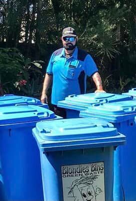 A Man Is Standing Next To A Row Of Blue Trash Cans — Blondies Bins in East Mackay, QLD