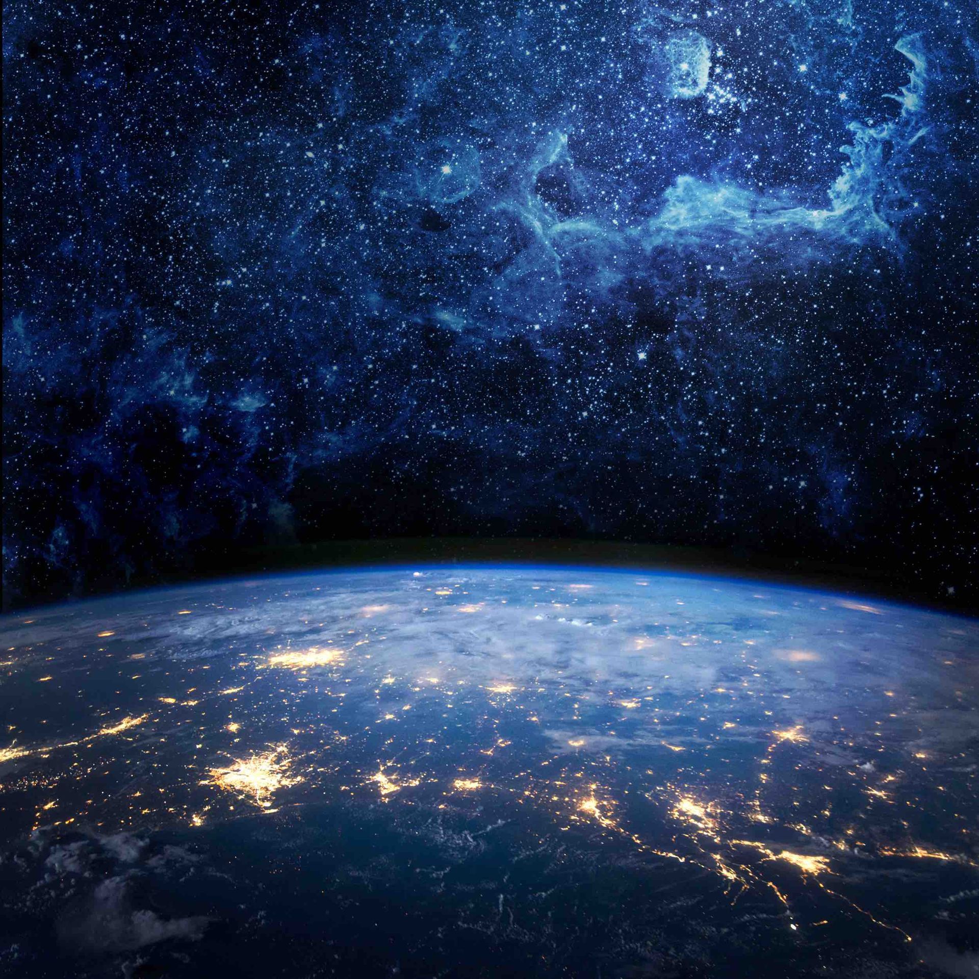 Earth at night, city lights visible from space, with a starry, nebulous night sky above.