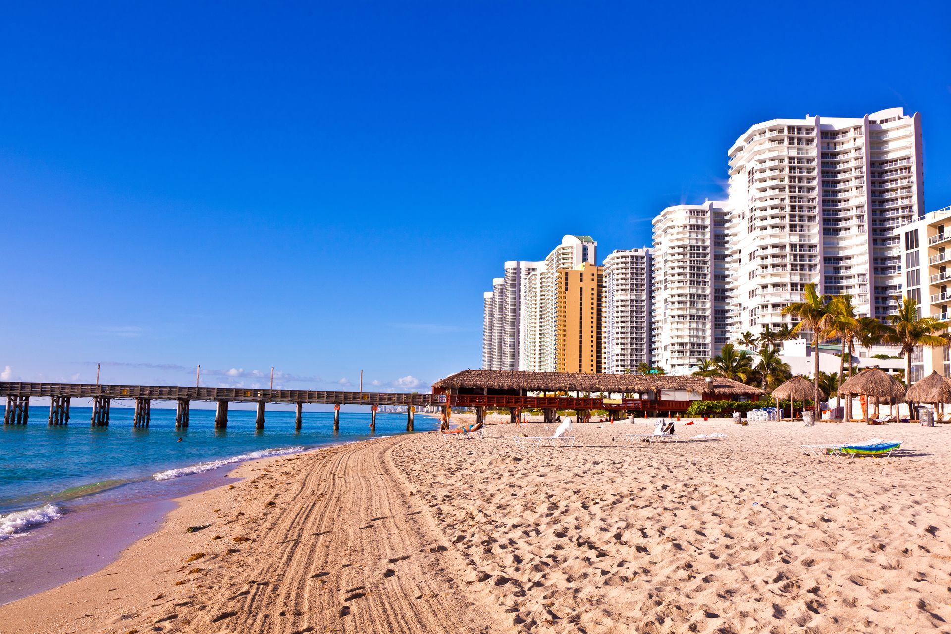 A beach with a pier and tall buildings in the background.