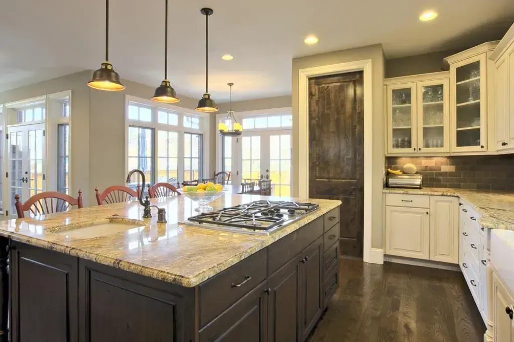 Modern kitchen with large island, pendant lights, white cabinets, and dark wood flooring