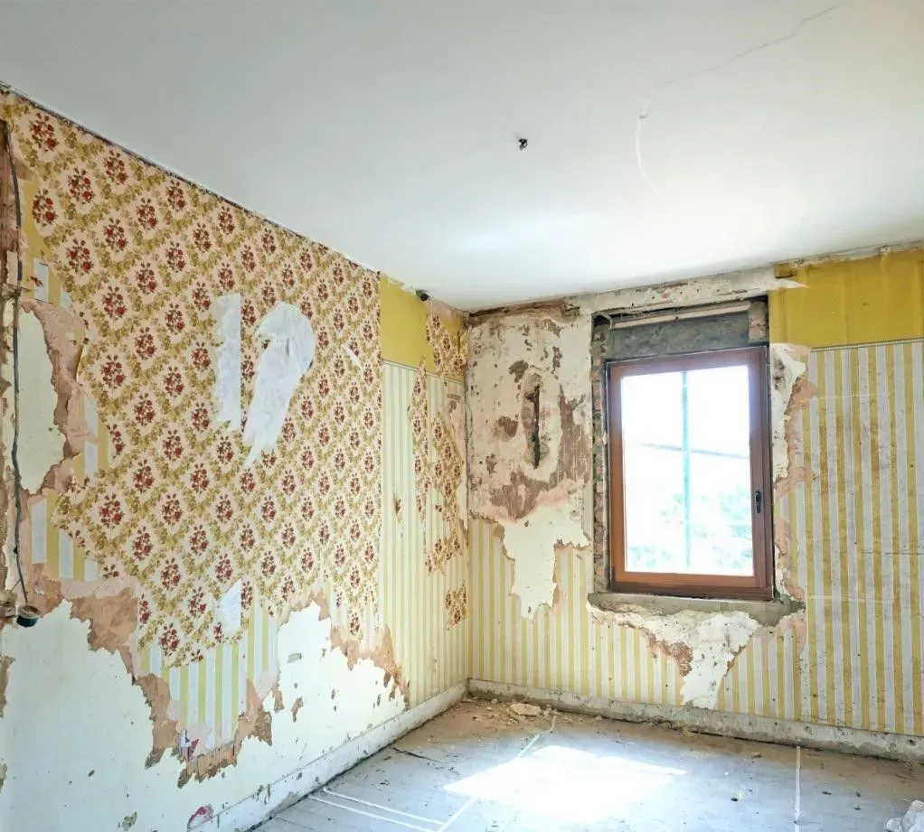 An empty room with peeling wallpaper and a window.