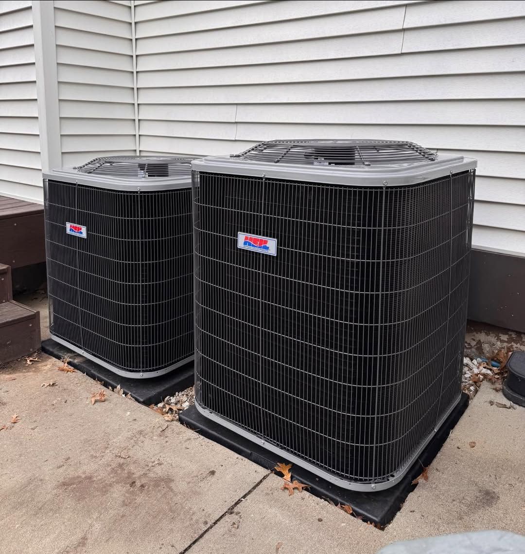 Two air conditioners are sitting on the sidewalk in front of a house.