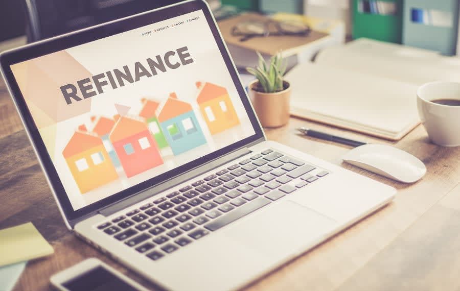 A laptop computer is sitting on a wooden desk with the word refinance on the screen.