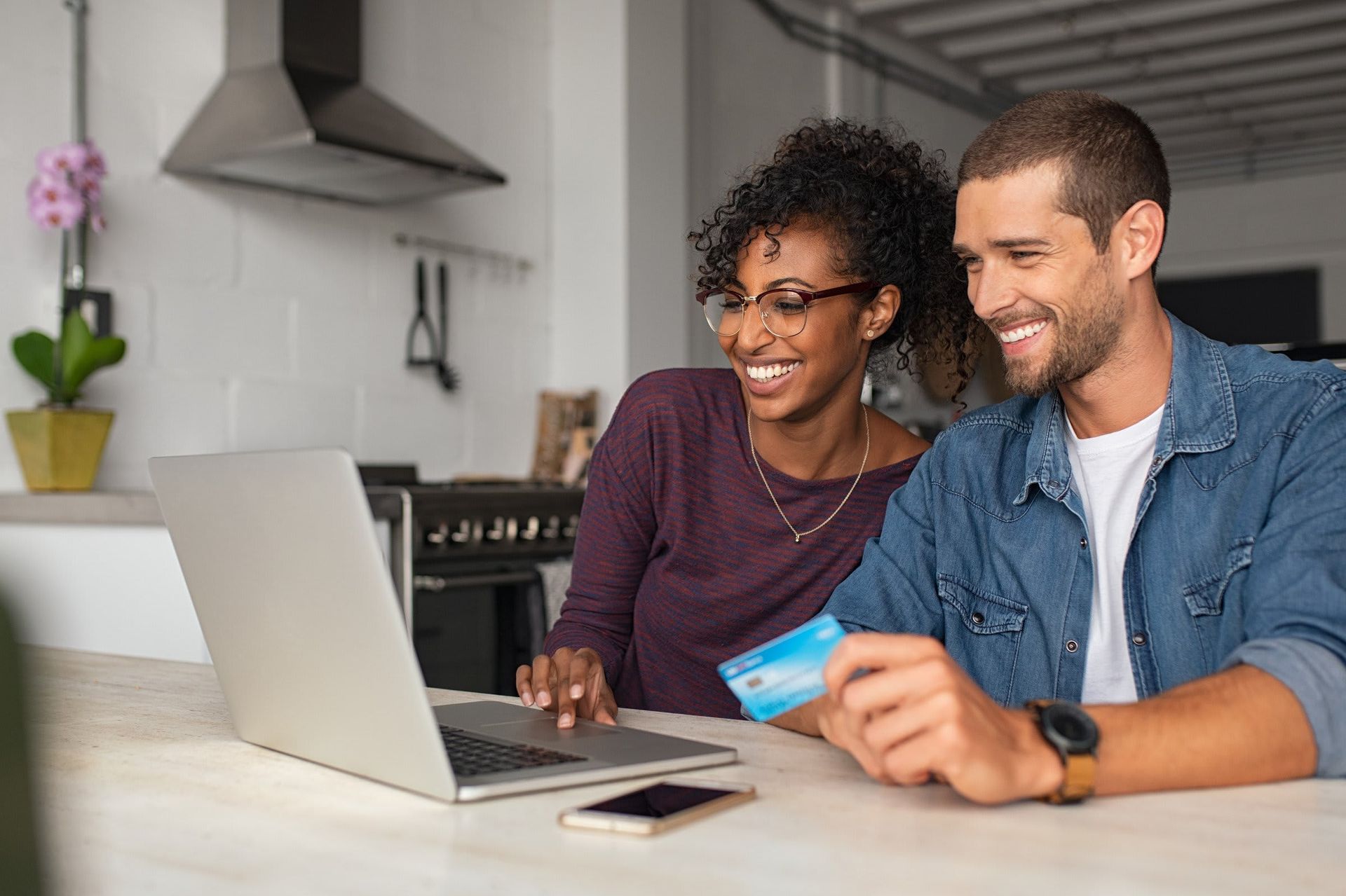 A man and a woman are sitting at a table using a laptop and a credit card.