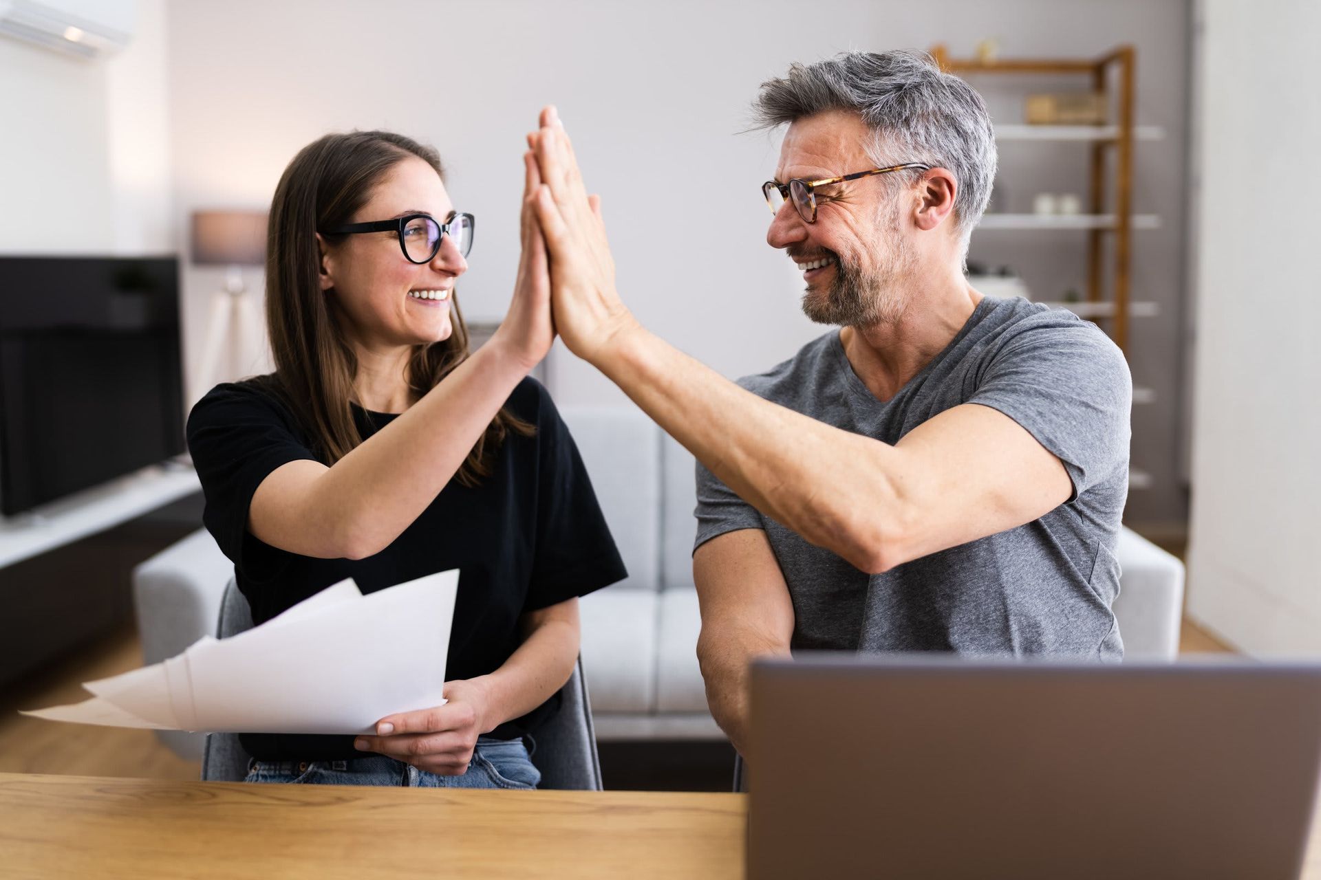 A man and a woman are giving each other a high five in front of a laptop.