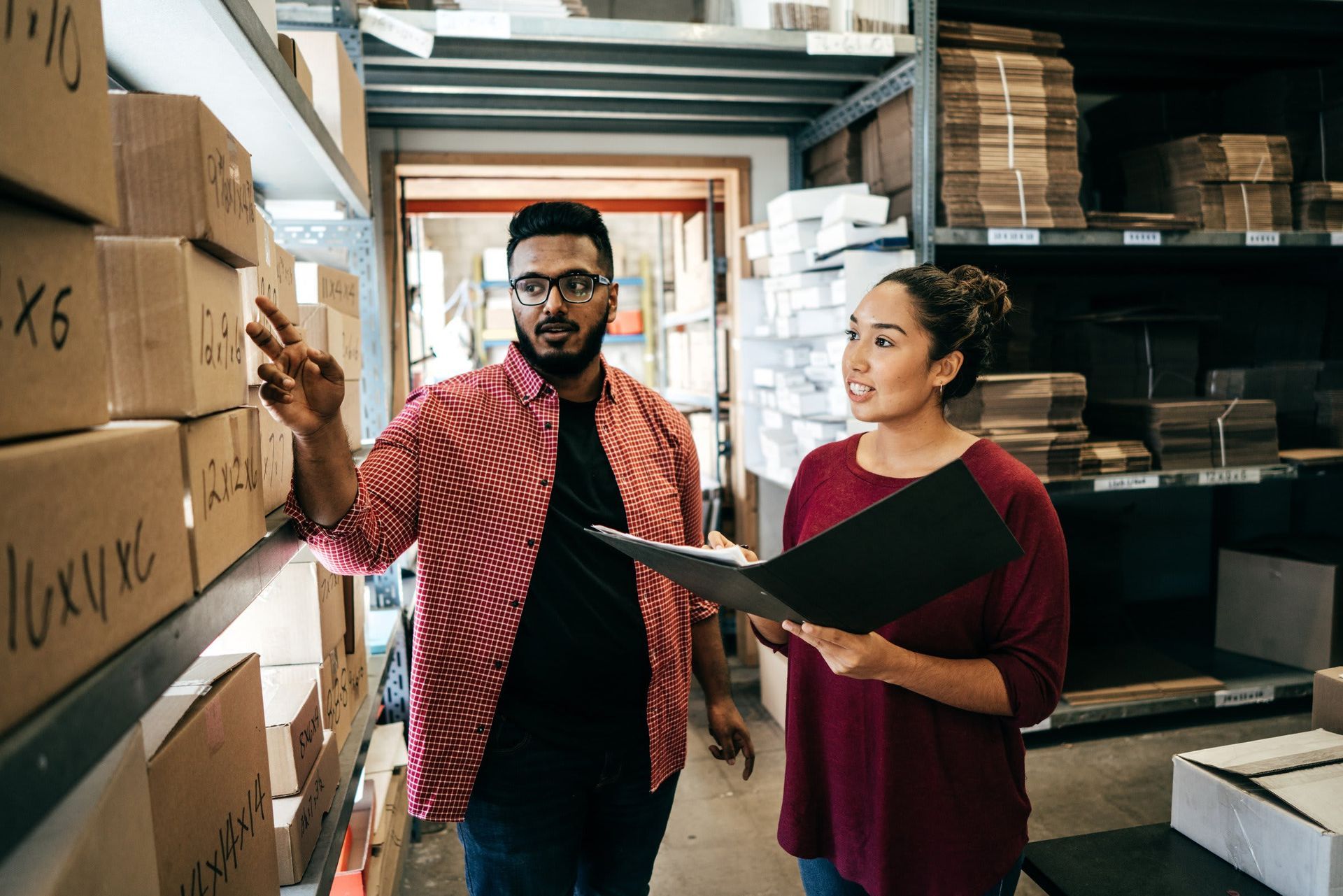 A man and a woman are looking at boxes in a warehouse.