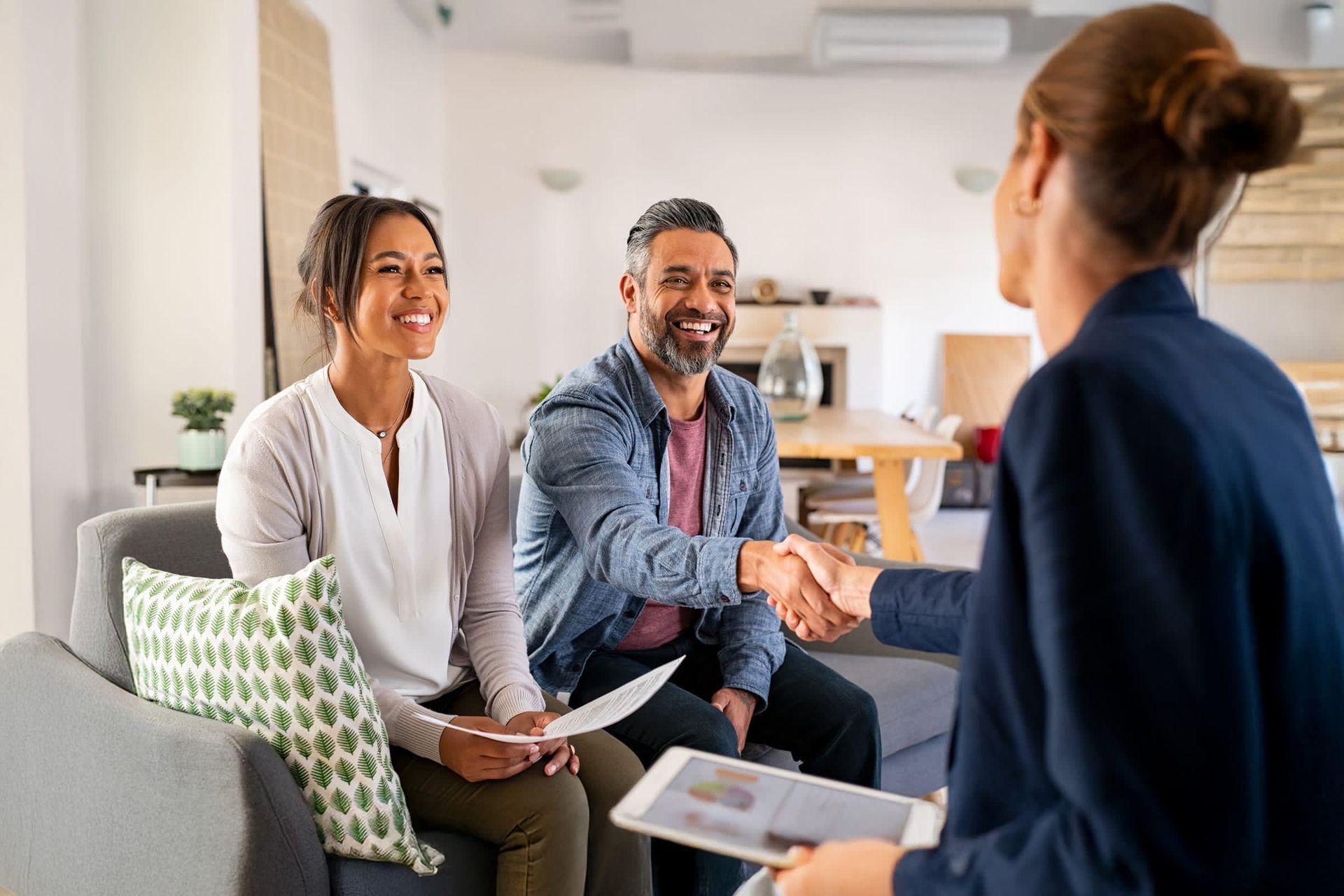 A man and woman are shaking hands with a real estate agent while sitting on a couch.