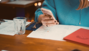 A woman is sitting at a table using a cell phone.