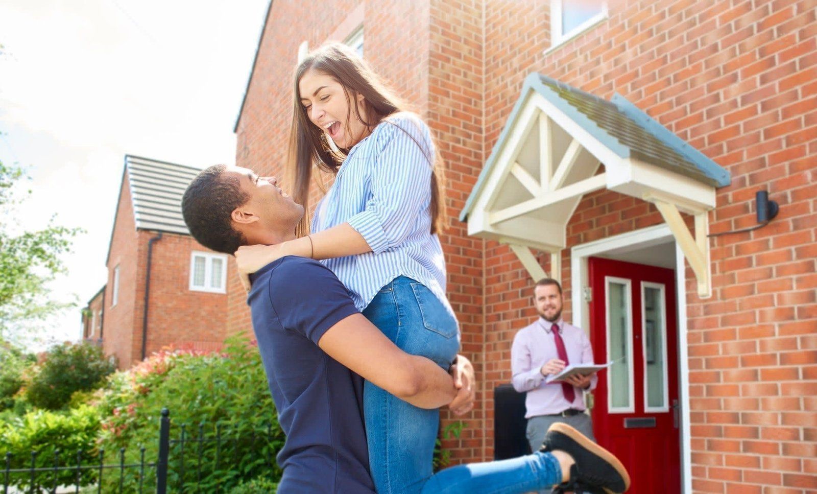 A man is holding a woman in his arms in front of a house.