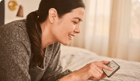 A woman is laying on a bed using a cell phone.