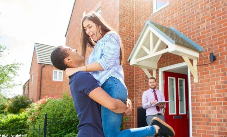 A man is holding a woman in his arms in front of a house.