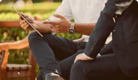 Two men are sitting on a bench looking at a tablet.