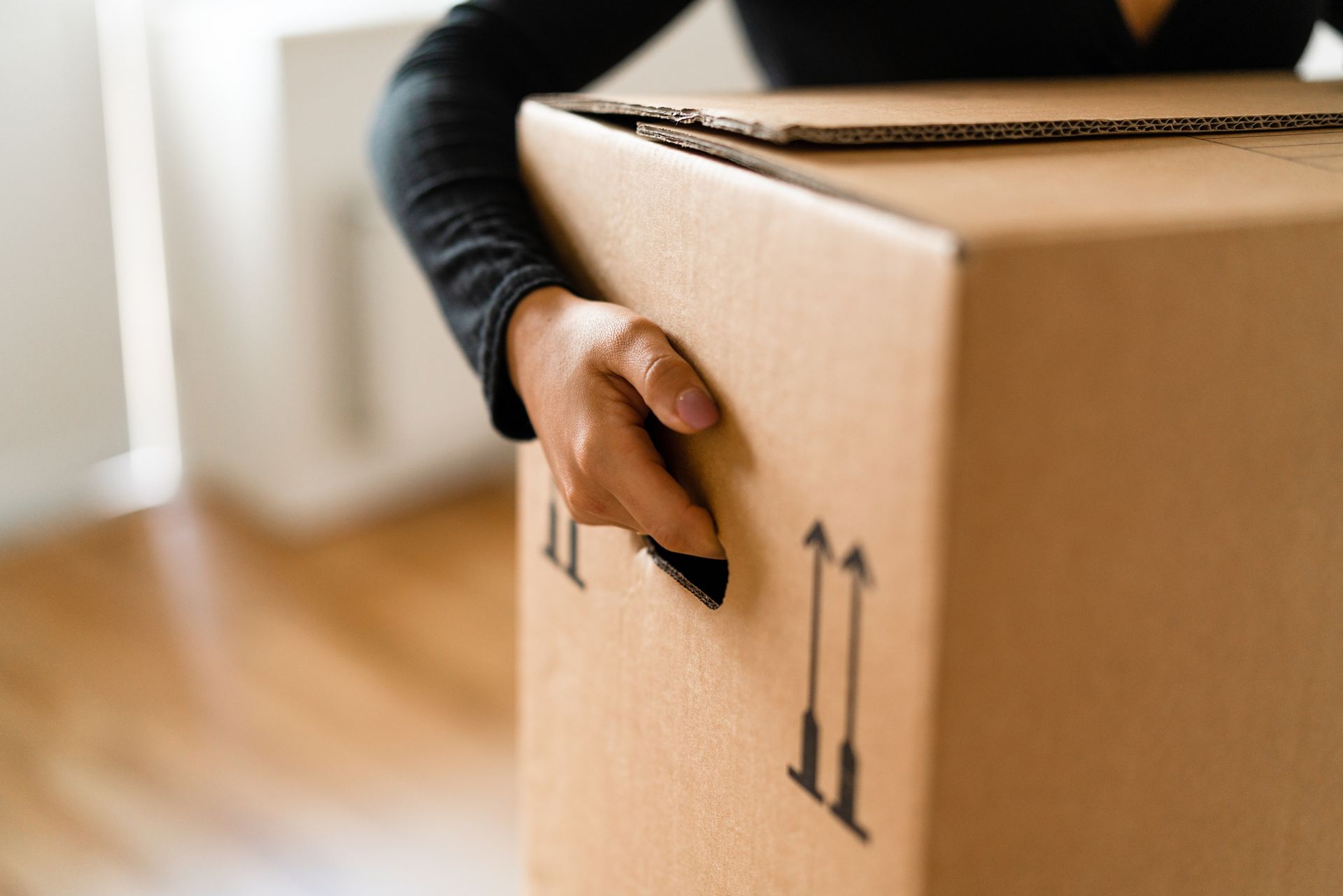 A woman is carrying cardboard moving boxes into her new home.