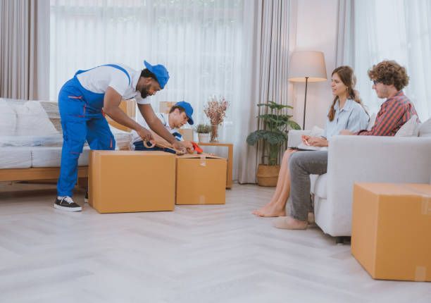 Movers taping boxes as a couple watches in the living room.