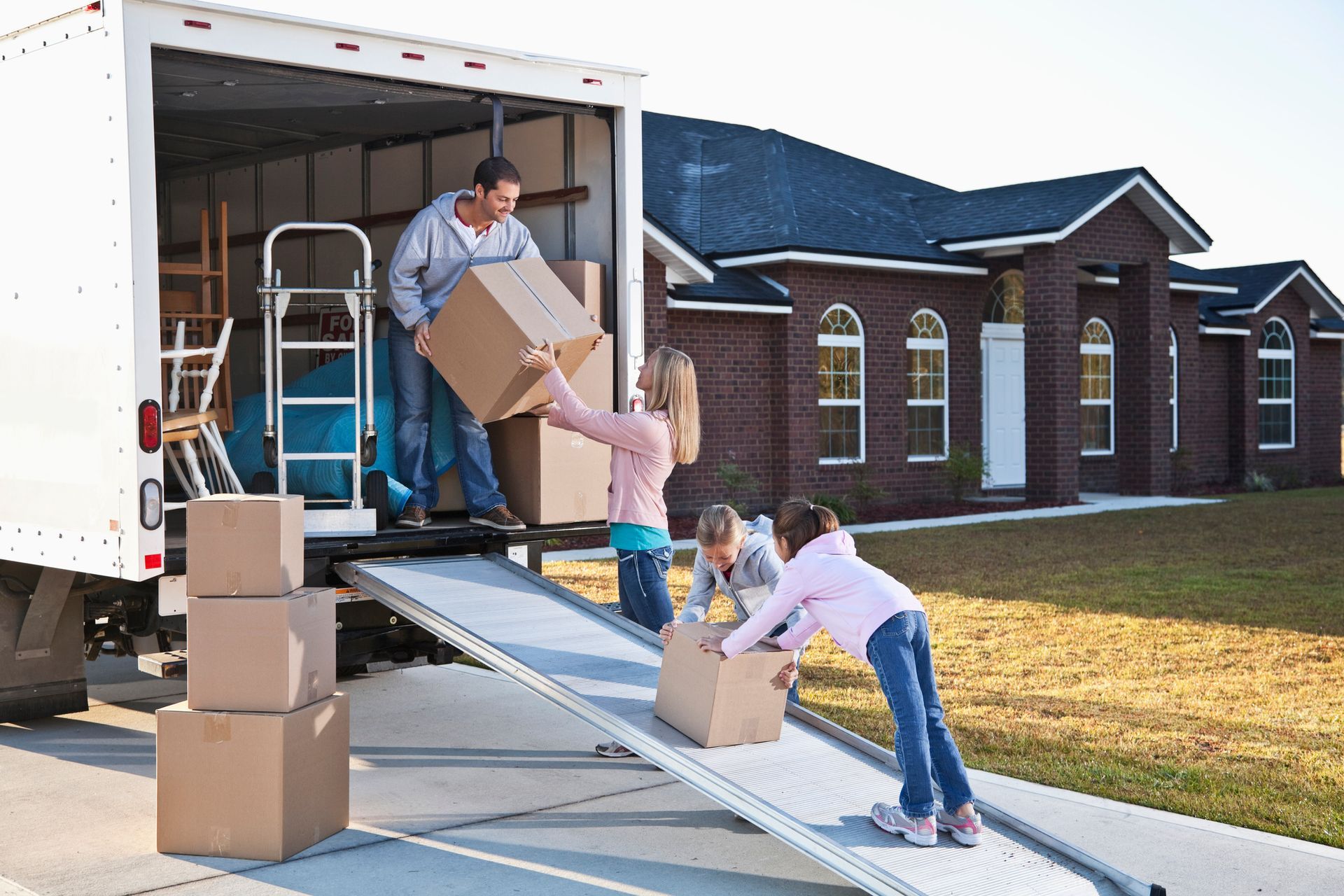 Family of 4 unloads brown boxes from moving van, showcasing residential moving services.