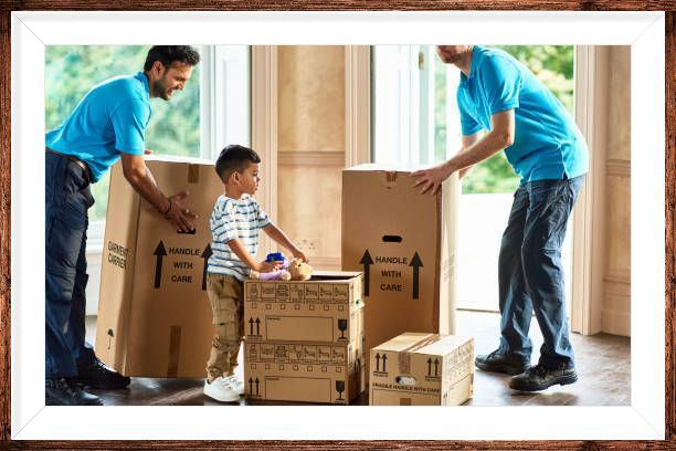 Two movers in blue shirts assist a child with unpacking boxes in a sunlit room.