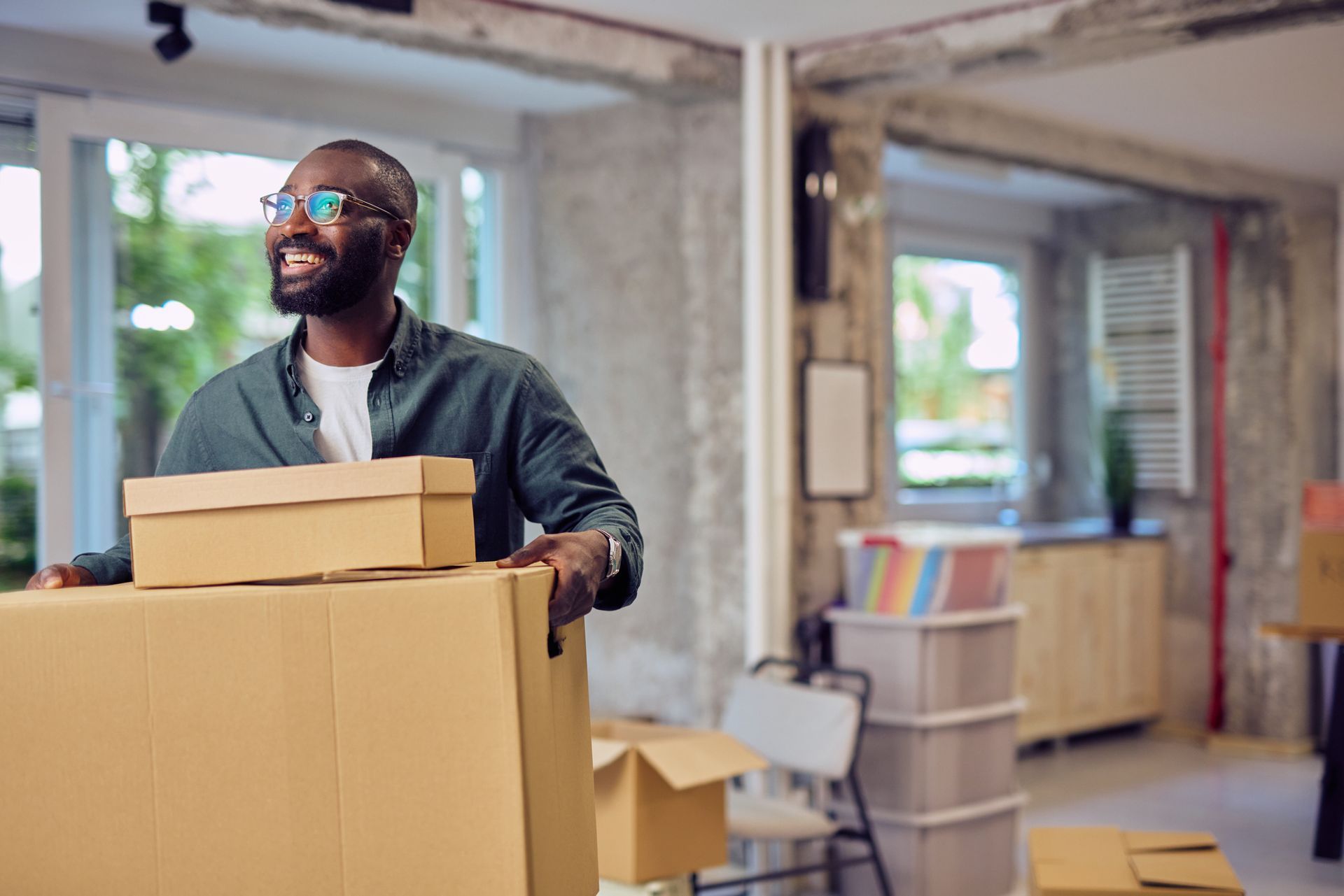 Smiling businessman carrying cardboard boxes in new office during relocation.