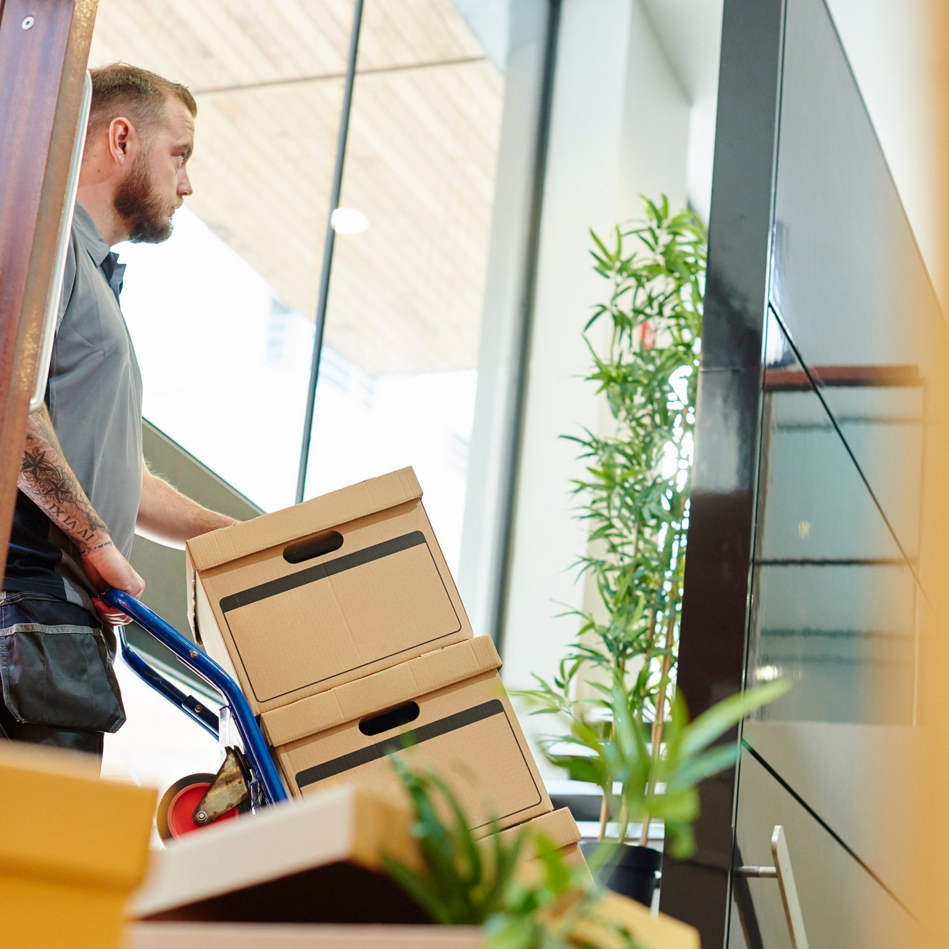 A man pushes a trolley of office boxes through the door of a modern office during a move.