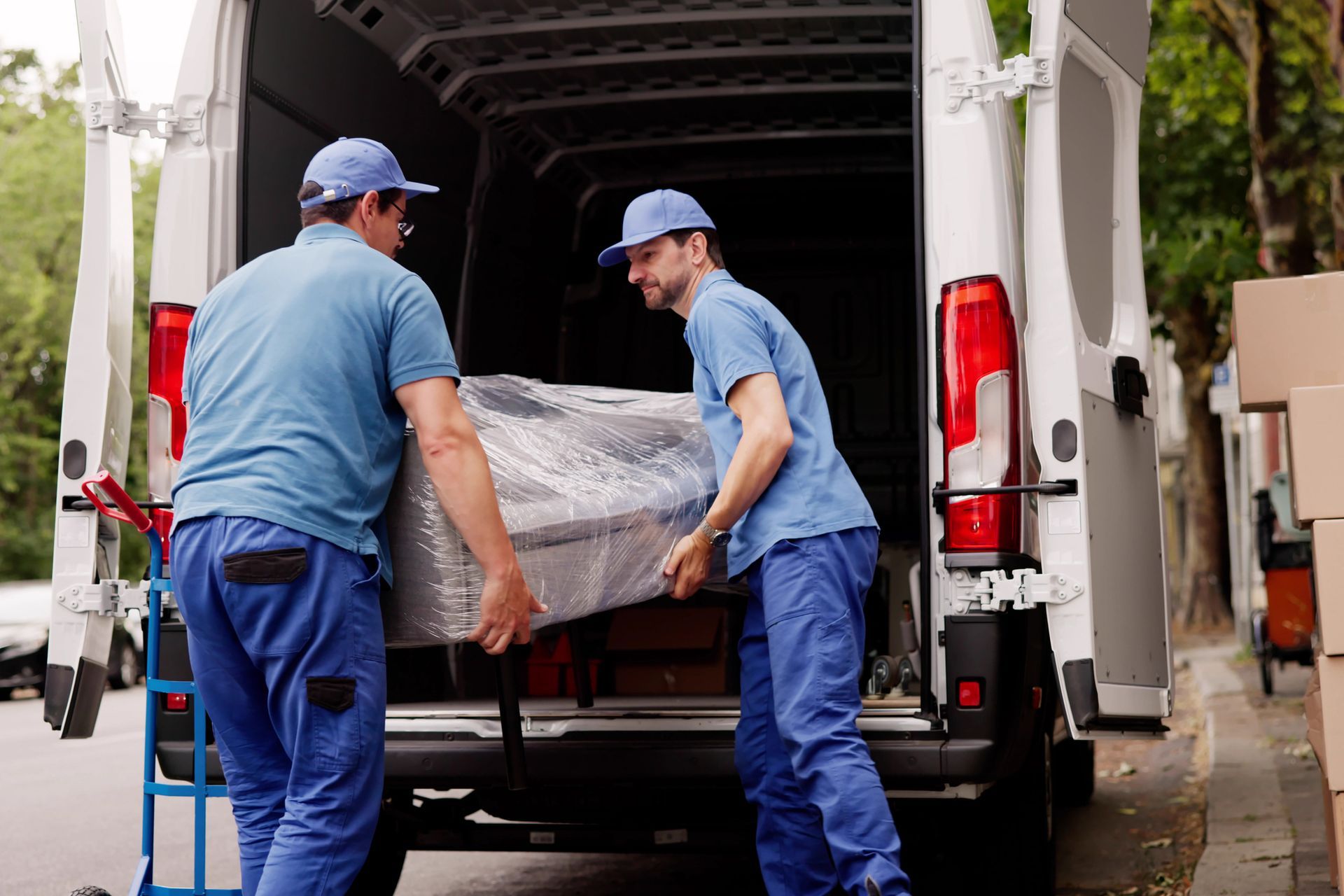 Two workers load a wrapped piece of furniture into a white moving van.