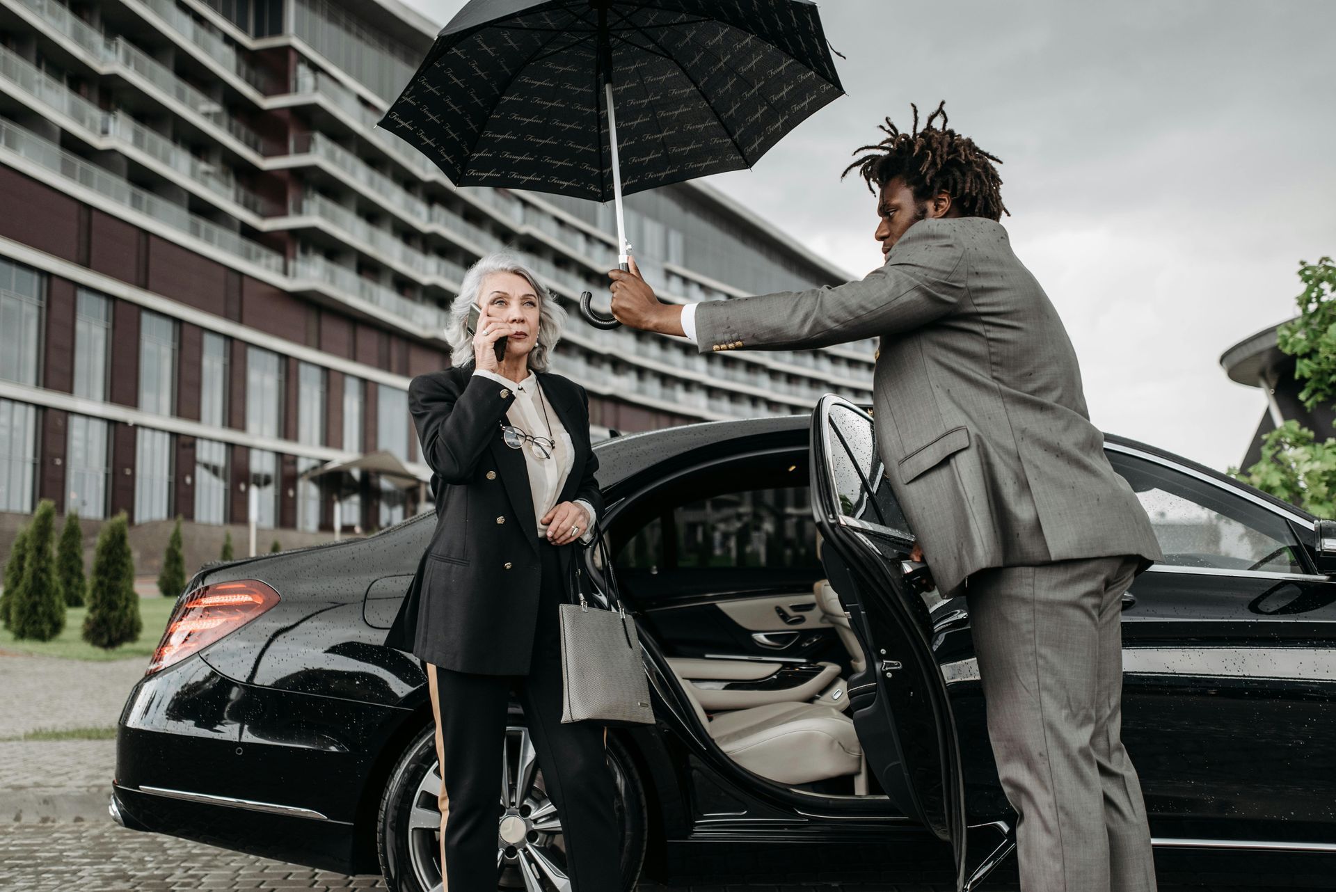 A man is holding an umbrella over a woman getting out of a car.