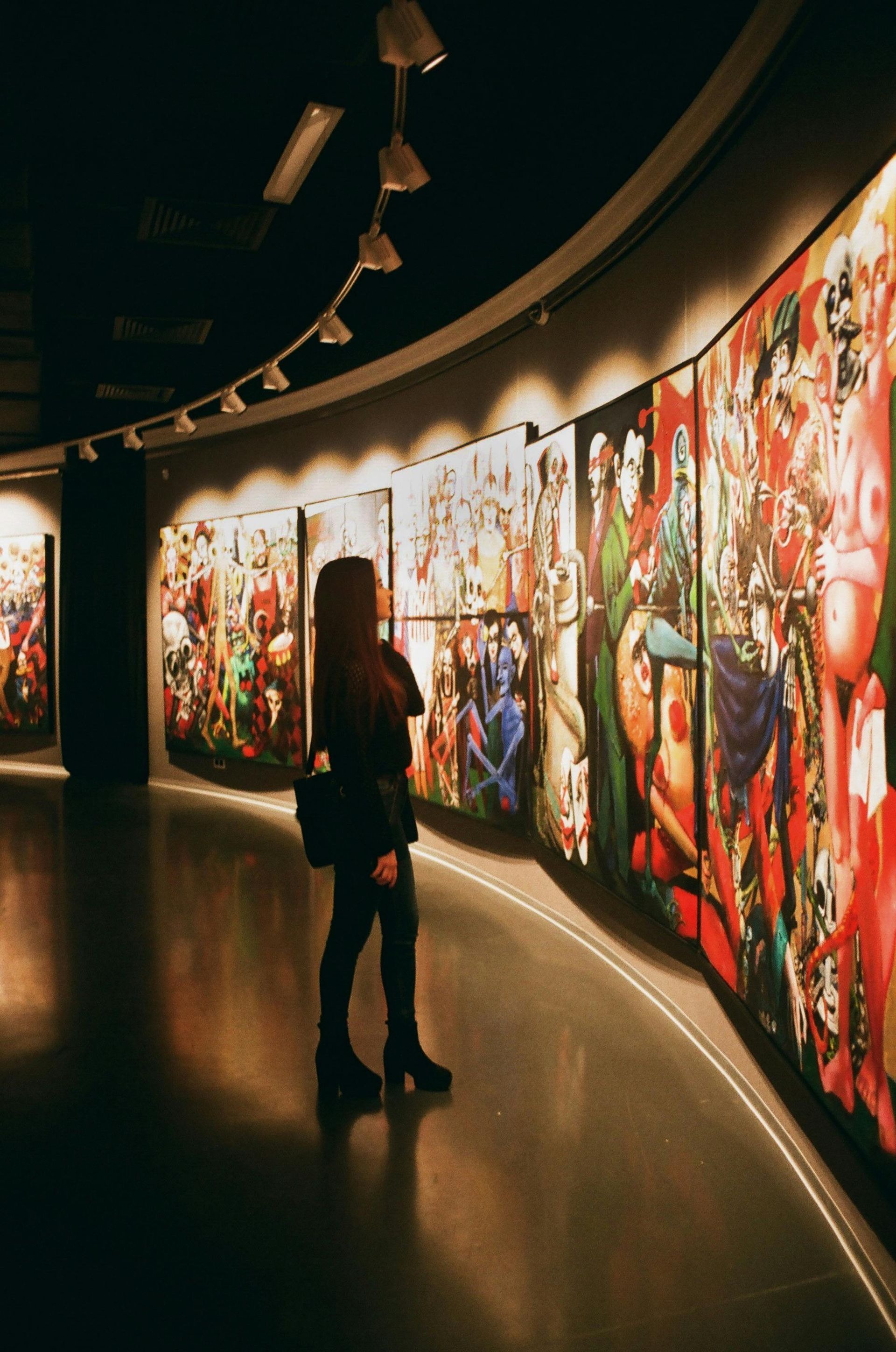 A woman is standing in front of a wall of paintings in a museum.