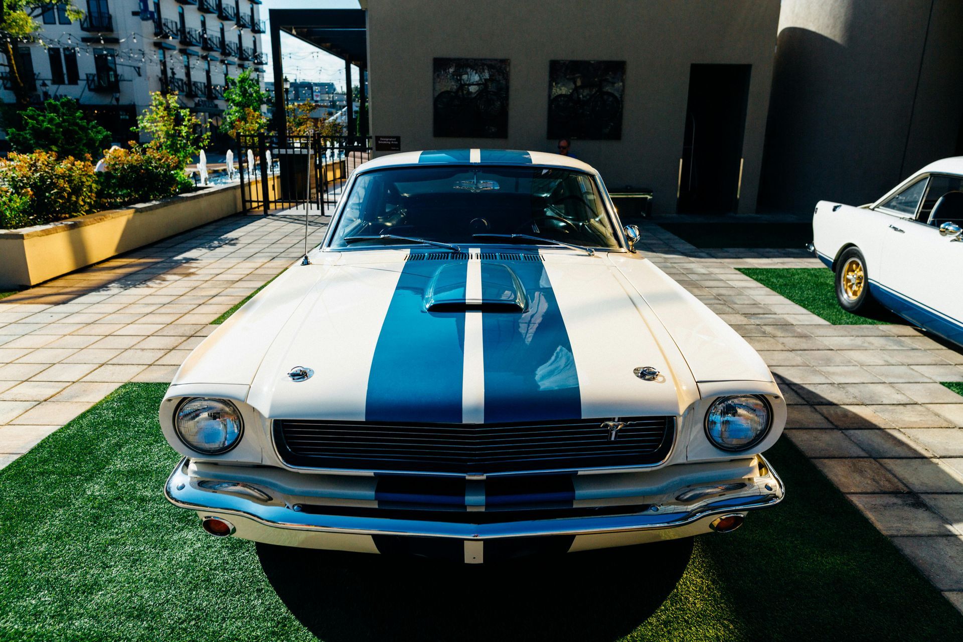 A white mustang with blue and white stripes is parked in front of a building.