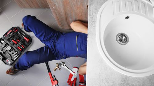 A plumber is laying on the floor next to a sink.