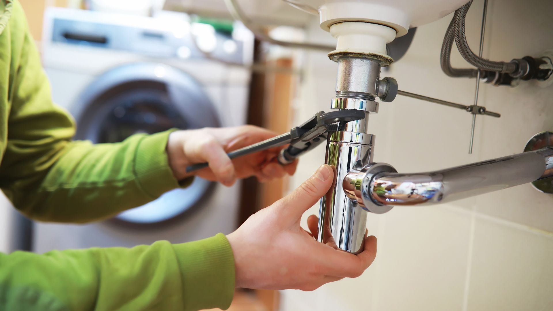 A plumber is fixing a sink with a wrench.
