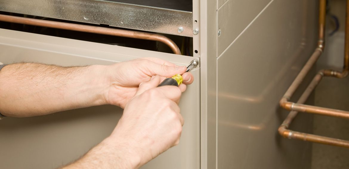 A man is working on an air conditioner with a screwdriver.