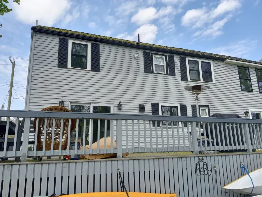 A white house with black shutters is behind a wooden fence.