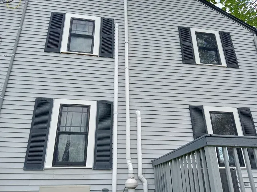 A gray house with black shutters and a white pipe on the side.