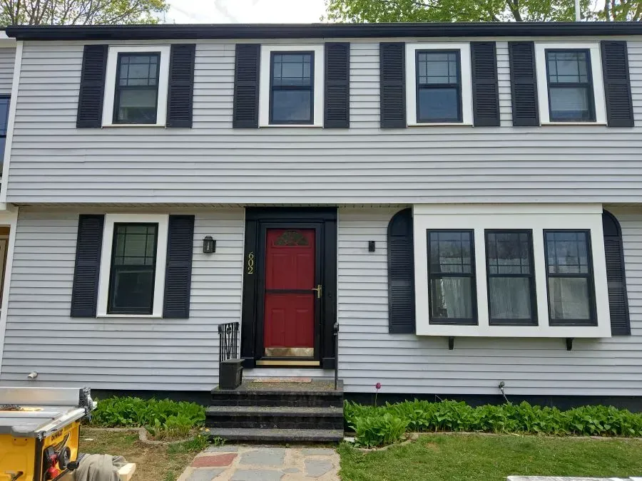A white house with black shutters and a red door.
