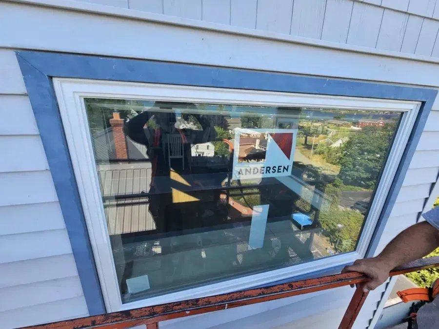 A man is standing on a ladder next to a window on the side of a house.
