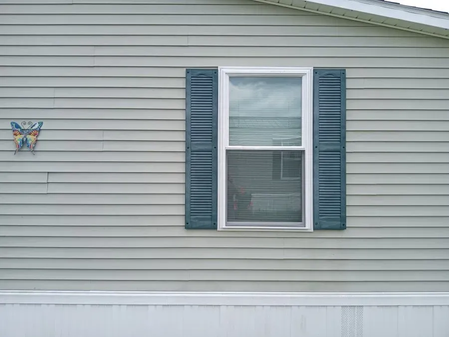 A mobile home with a window and blue shutters on the side.