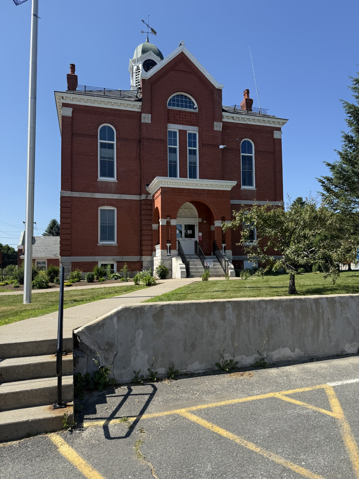 Red brick courthouse with white trim and a clock tower, in a sunny setting.