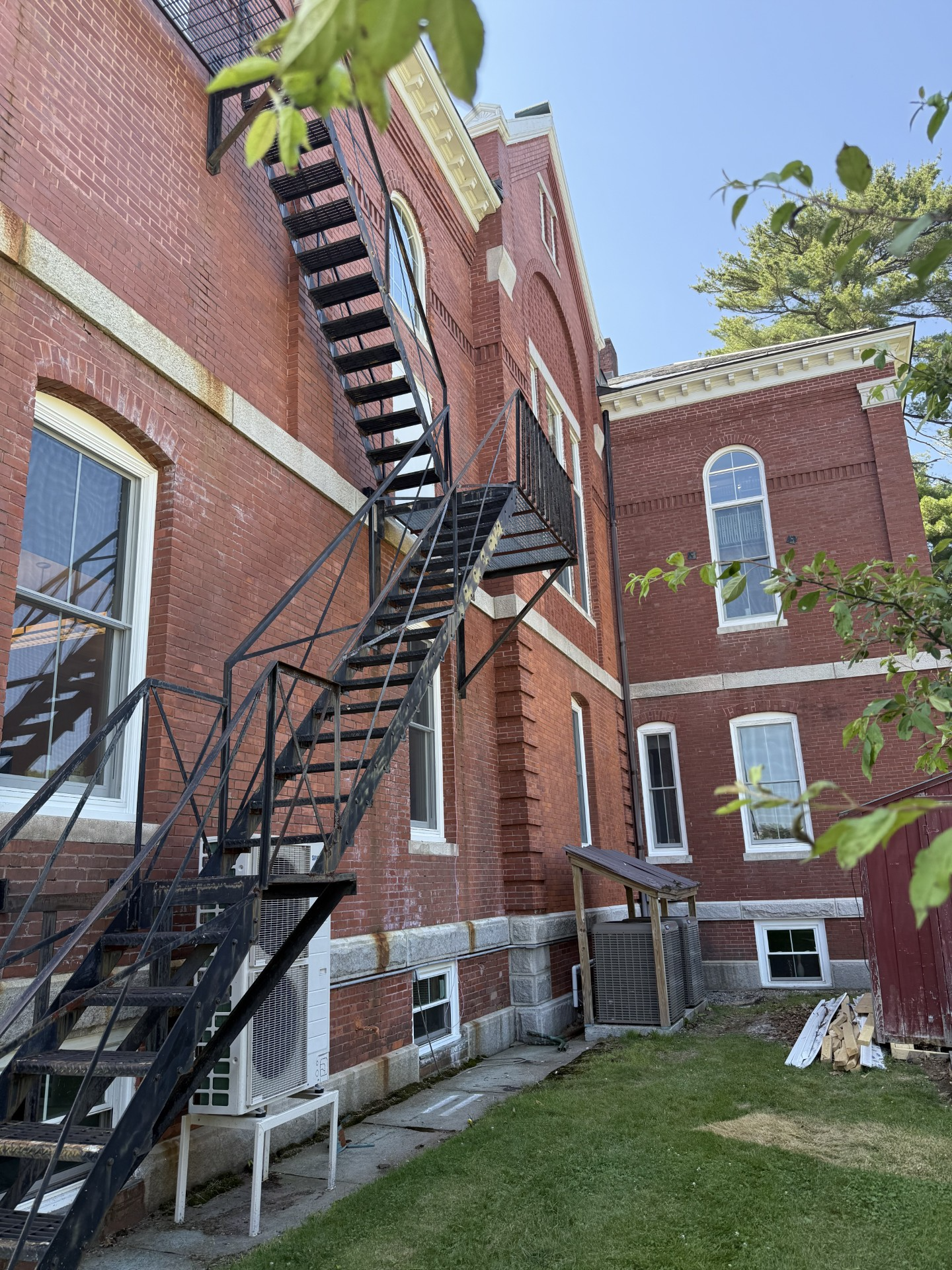 Brick building exterior with black metal fire escape. Green grass and blue sky.