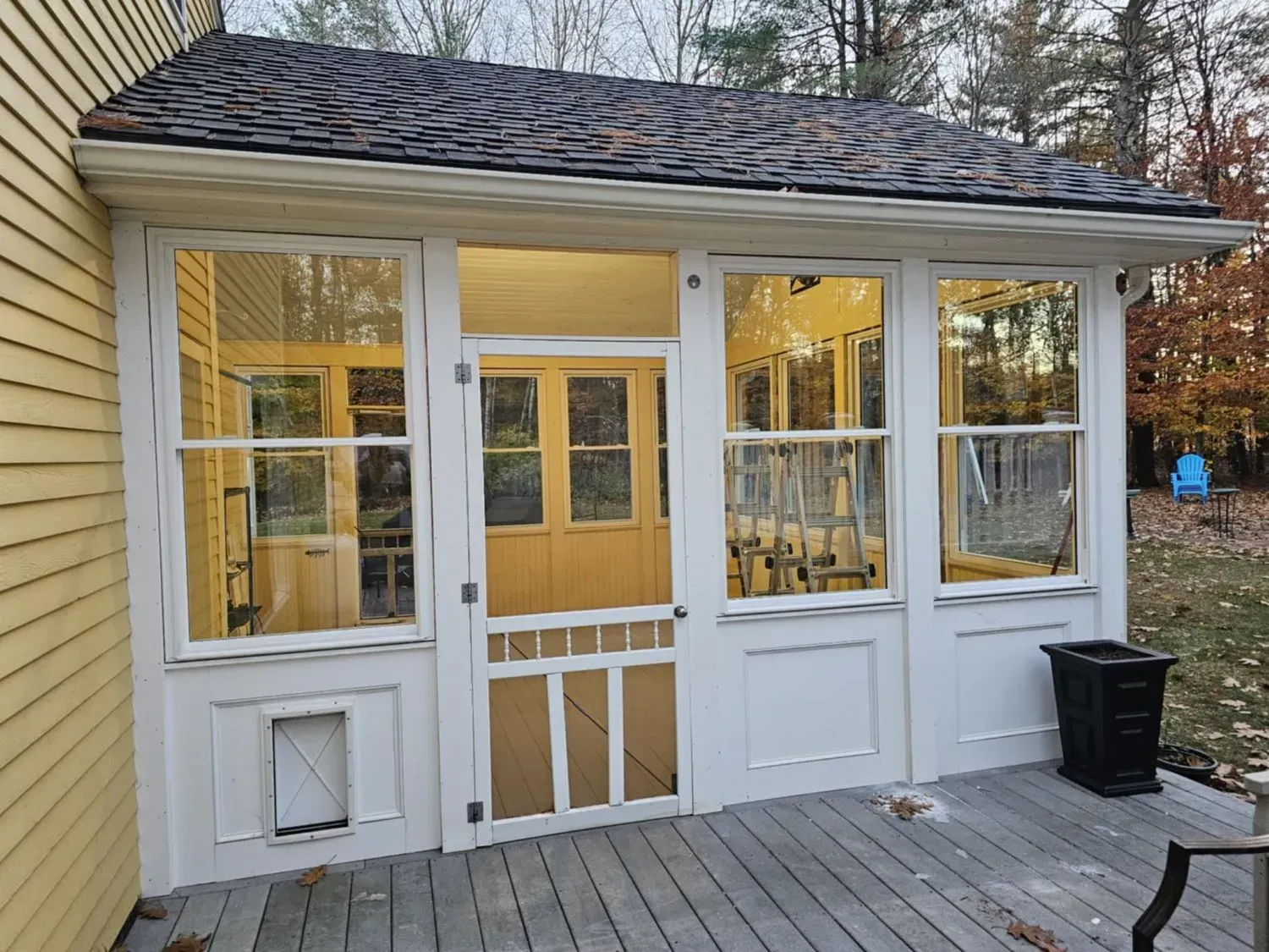 A screened in porch with a yellow house in the background.