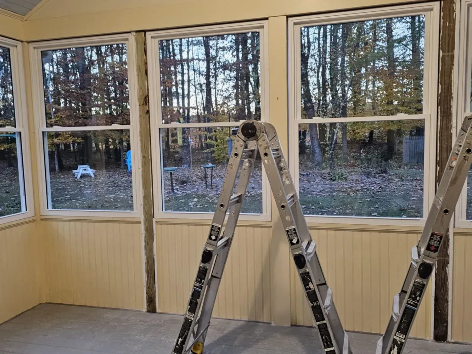 A ladder is sitting in a room with a lot of windows.