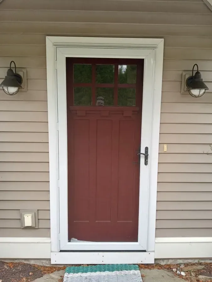A red door with a white frame is on the side of a house.