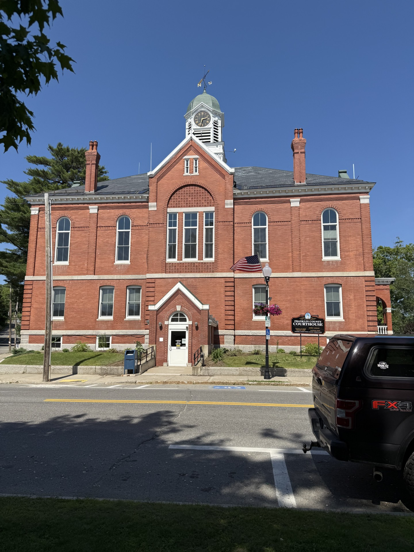 Red brick courthouse with clock tower under a clear blue sky. A black truck is parked in front.