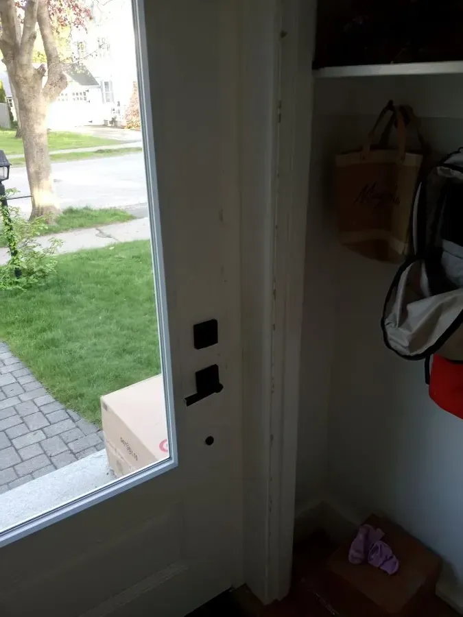 A white door with a black handle is open to a yard