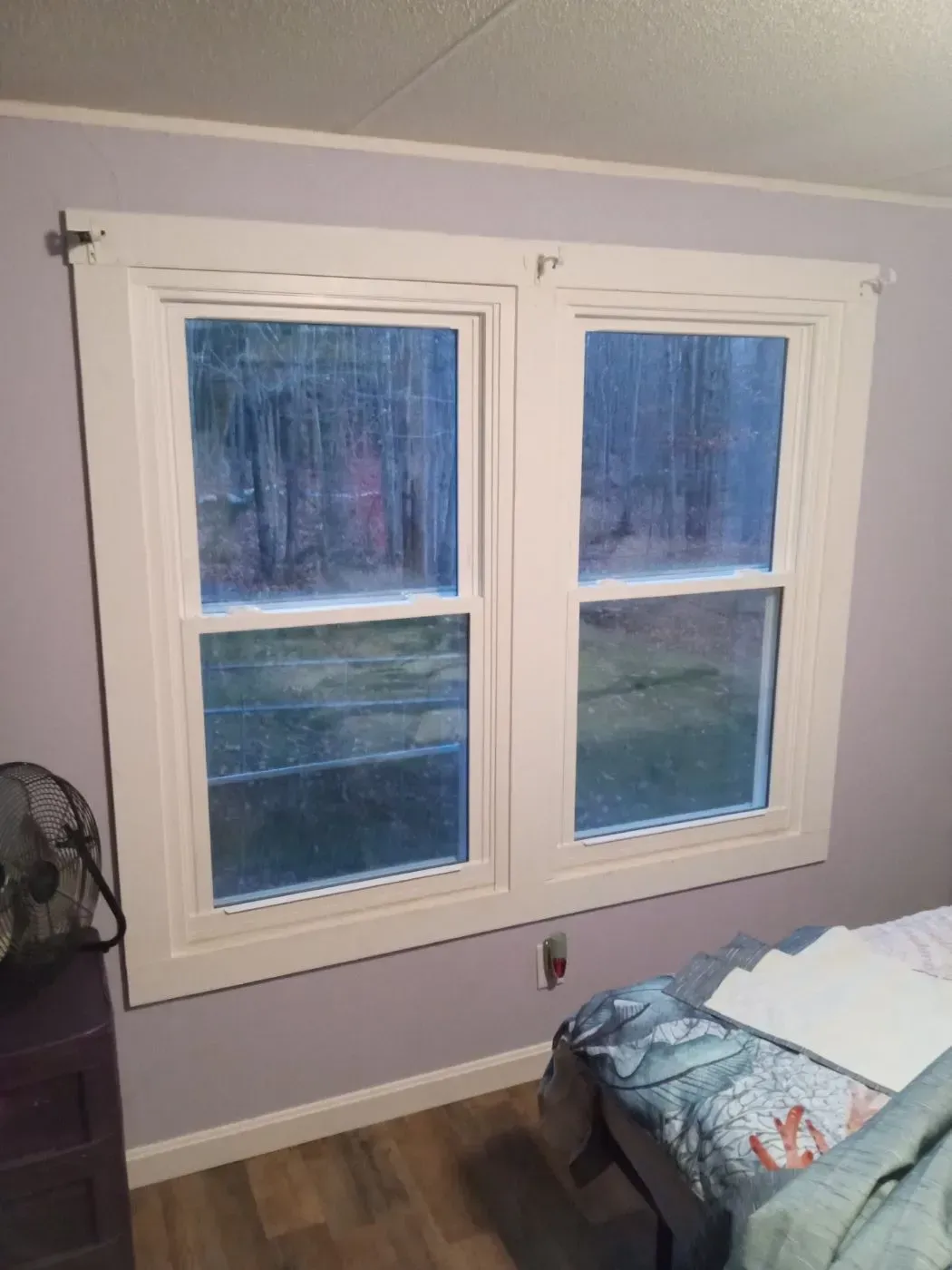 A bedroom with two windows and a bed.